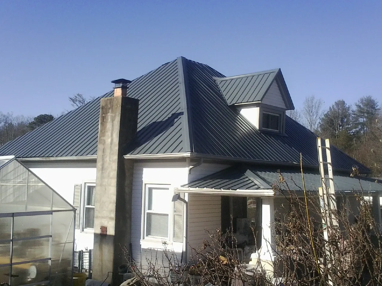 Dark blue standing seam metal roof on a white farmhouse with dormer — Slate & Tile Roof Repair by Roofing Brothers in Bayard