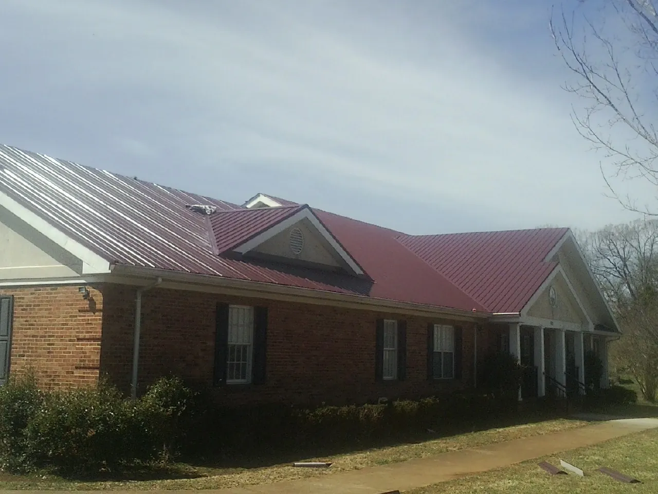 Red metal roof with gabled entries on a long brick building, from a Hail Damage Roof Repair job in Bayard