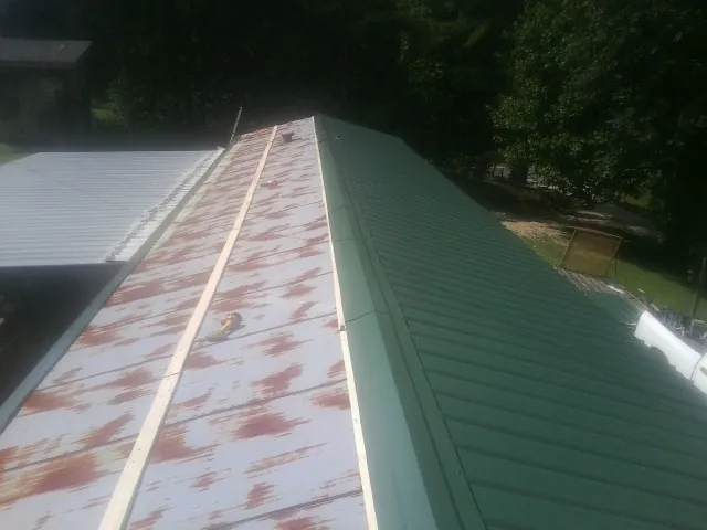 Old rusted panels beside newly installed green metal roofing — Wind Damage Roof Repair by Roofing Brothers in Bayard