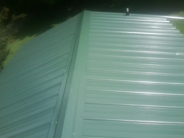 New green metal panels meeting at the ridge of a roof — Flat Roof Repair work by our crew in Bayard