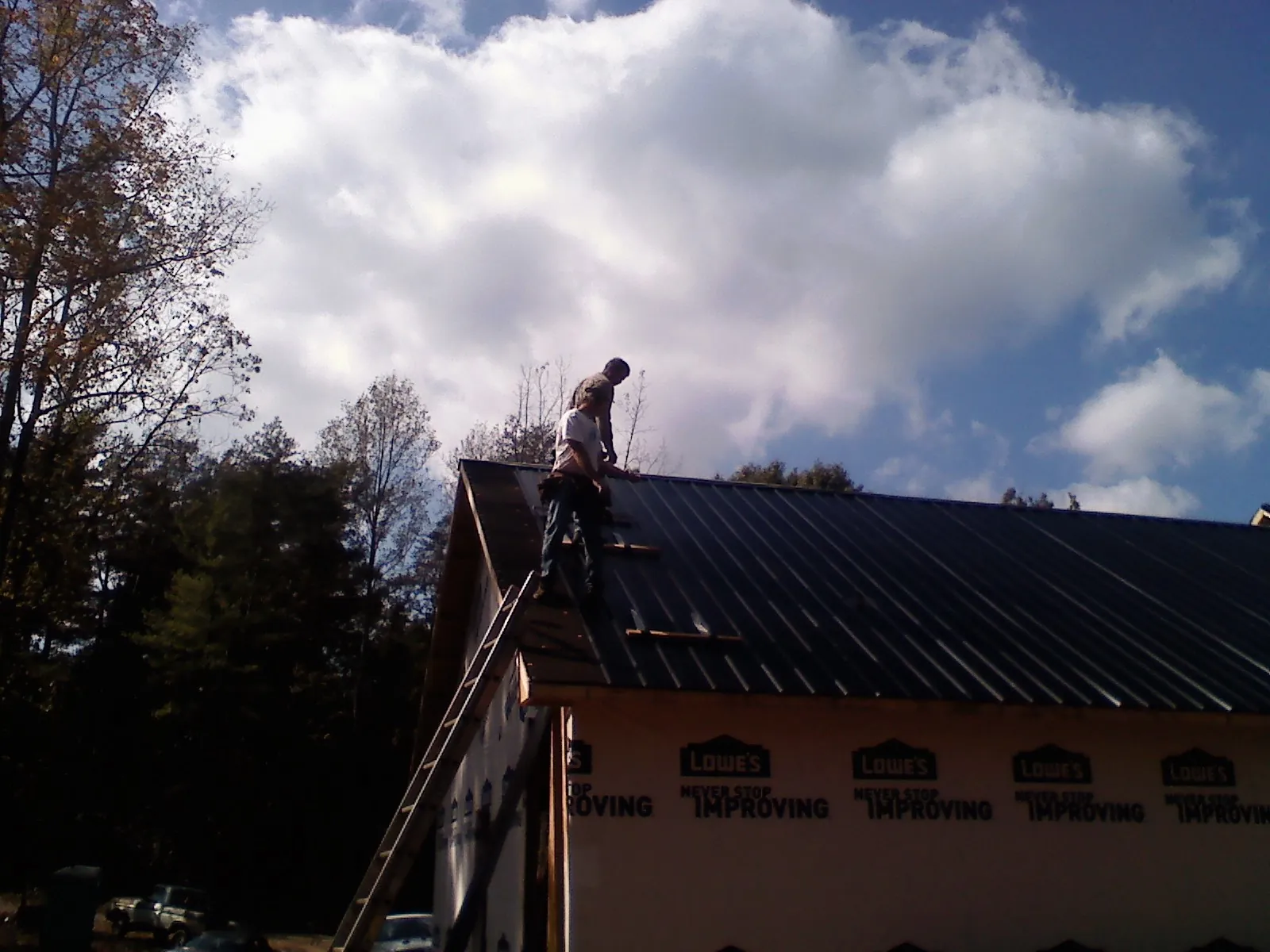 Roofer fastening dark metal panels high against a cloudy sky, from a Roof Inspection job in Bayard