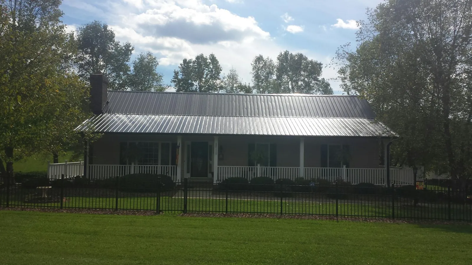 Gray metal roof on a brick ranch with a full width front porch — Gutter Guard Installation work by our crew in Bayard