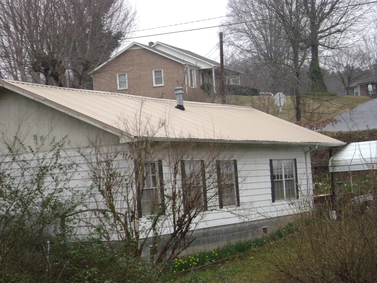 Tan metal roof on a white sided house set into a hillside — Commercial Roofing by Roofing Brothers in Bayard