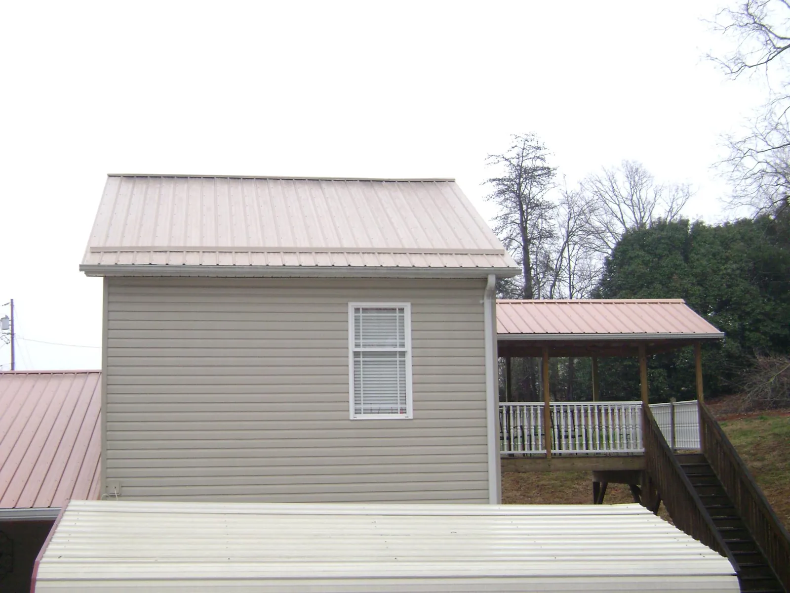 Tan metal roofs on a two story addition and attached porch in Bayard